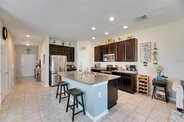 kitchen with visible vents, dark brown cabinets, light stone countertops, a breakfast bar, and stainless steel appliances