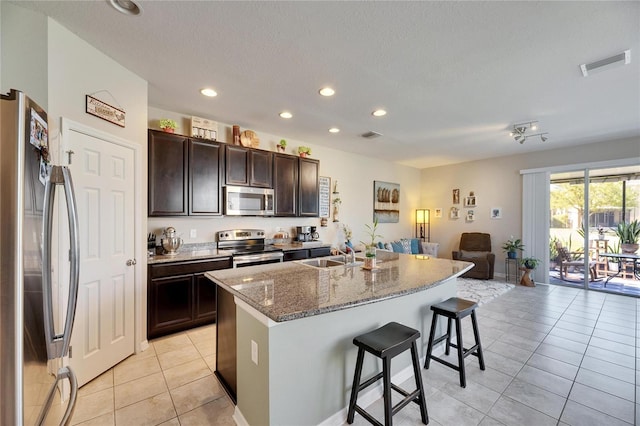 kitchen with visible vents, open floor plan, a kitchen bar, light tile patterned floors, and stainless steel appliances