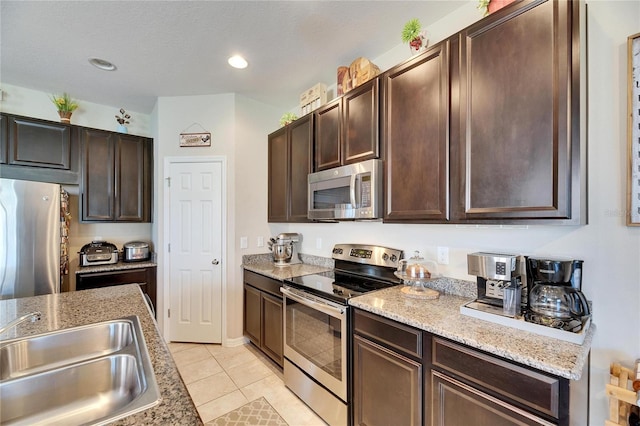 kitchen with a sink, appliances with stainless steel finishes, light tile patterned floors, and dark brown cabinets