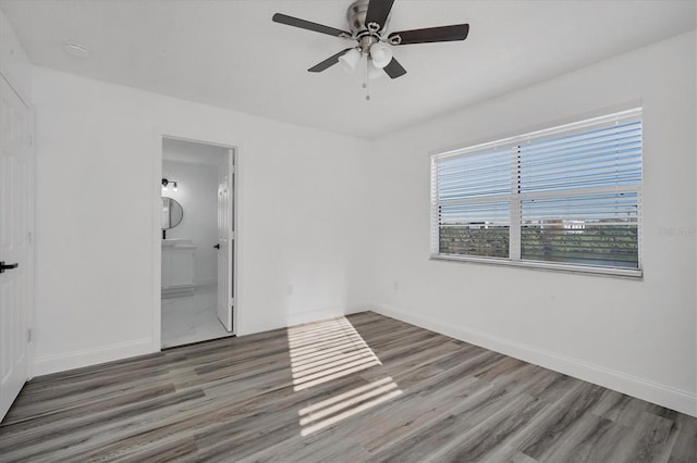 unfurnished bedroom with ceiling fan, ensuite bathroom, baseboards, and wood finished floors