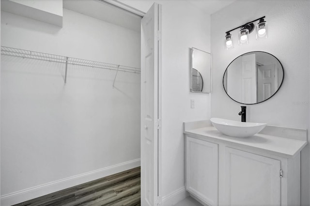 bathroom featuring a walk in closet, baseboards, wood finished floors, and vanity