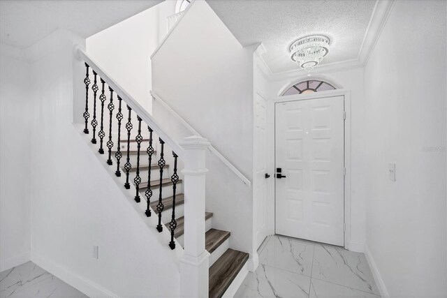 foyer entrance featuring crown molding, baseboards, an inviting chandelier, marble finish floor, and a textured ceiling