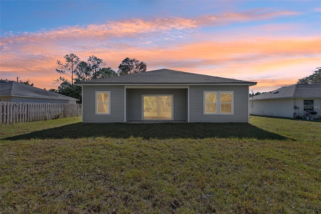 back of house at dusk featuring a yard and fence