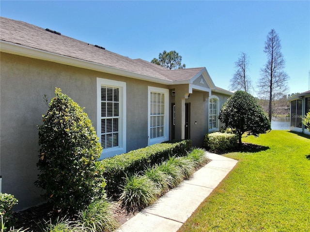 entrance to property with stucco siding, a lawn, and roof with shingles