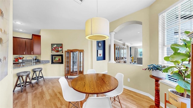 dining room with arched walkways, recessed lighting, baseboards, and light wood-style floors