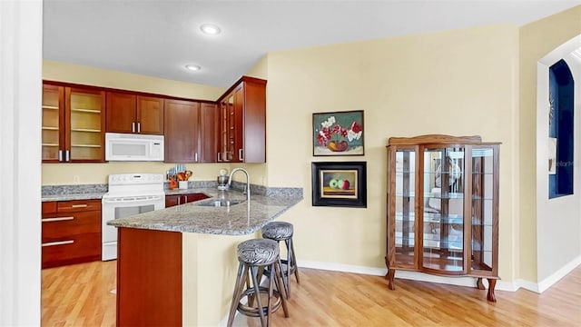 kitchen with a sink, white appliances, light wood-style floors, and arched walkways