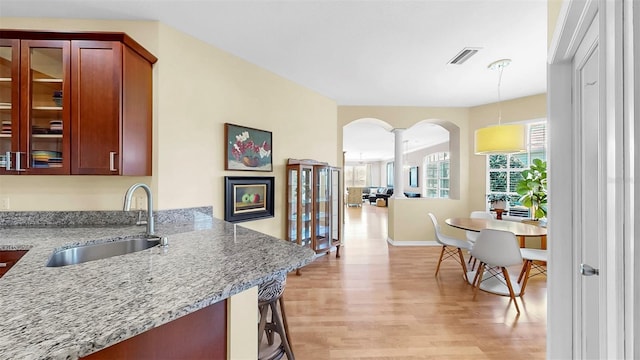 kitchen featuring visible vents, light wood-style flooring, a sink, light stone counters, and arched walkways