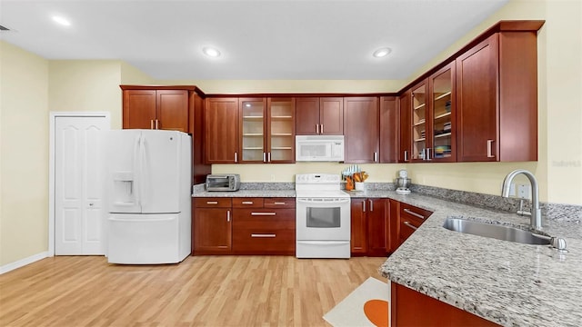 kitchen with light wood finished floors, white appliances, light stone countertops, and a sink