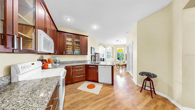 kitchen featuring light wood-type flooring, a sink, light stone counters, white appliances, and a peninsula