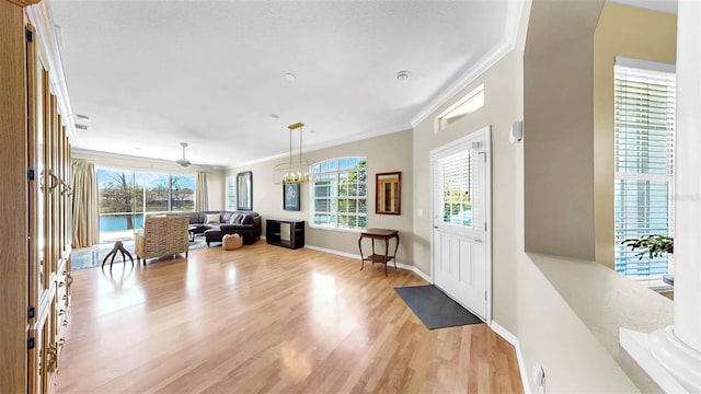 entryway with crown molding, ceiling fan with notable chandelier, baseboards, and light wood finished floors