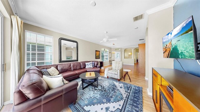 living room with visible vents, ornamental molding, a ceiling fan, light wood-style flooring, and arched walkways