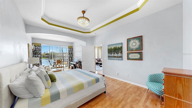 bedroom with access to outside, a tray ceiling, wood finished floors, arched walkways, and baseboards