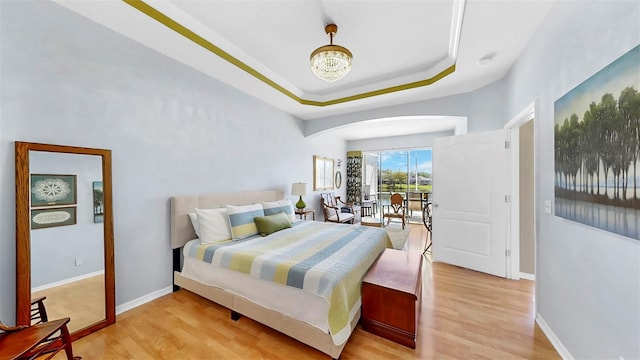 bedroom featuring an inviting chandelier, a tray ceiling, light wood-style floors, and baseboards