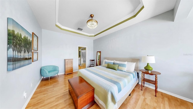 bedroom featuring a raised ceiling, wood finished floors, visible vents, and baseboards