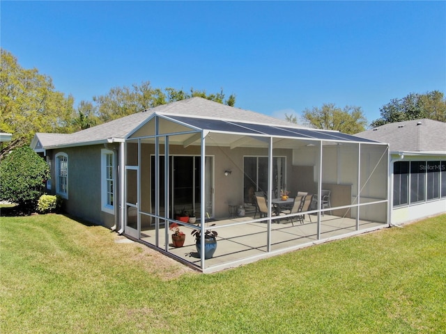 rear view of property with stucco siding, a lawn, a patio, roof with shingles, and a lanai