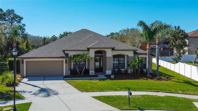 french country style house with a front yard, fence, driveway, stucco siding, and a garage