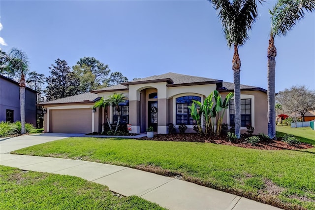 mediterranean / spanish-style home featuring stucco siding, an attached garage, concrete driveway, and a front lawn