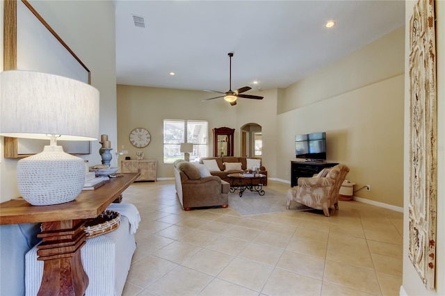 living area featuring visible vents, ceiling fan, a towering ceiling, light tile patterned flooring, and arched walkways