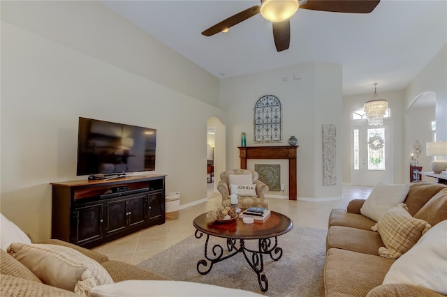 living room with arched walkways, light tile patterned flooring, a fireplace, and ceiling fan with notable chandelier