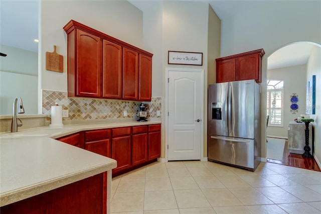 kitchen featuring stainless steel refrigerator with ice dispenser, a sink, tasteful backsplash, arched walkways, and dark brown cabinets