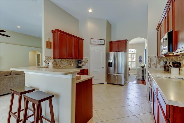 kitchen featuring open floor plan, arched walkways, a peninsula, appliances with stainless steel finishes, and dark brown cabinets