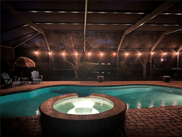 pool at night with a lanai, a pool with connected hot tub, and a patio