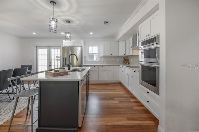 kitchen with crown molding, wall chimney exhaust hood, visible vents, and stainless steel appliances