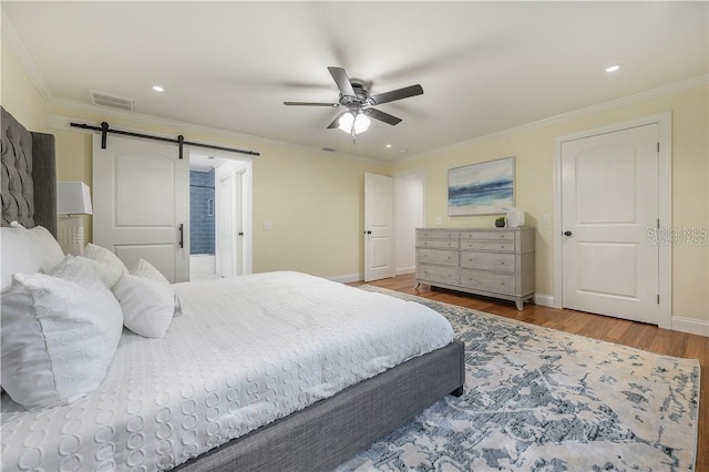 bedroom featuring a barn door, wood finished floors, crown molding, and baseboards