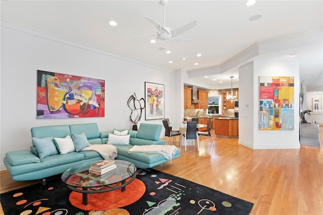 living room featuring crown molding, light wood-style flooring, a ceiling fan, and baseboards