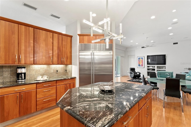 kitchen featuring backsplash, a center island, stainless steel built in fridge, light wood-style floors, and brown cabinetry