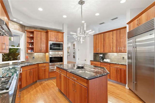 kitchen with a sink, built in appliances, a center island, and light wood finished floors