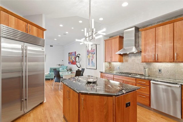 kitchen featuring dark stone counters, light wood-style flooring, appliances with stainless steel finishes, wall chimney exhaust hood, and backsplash