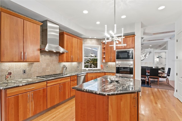 kitchen with wall chimney range hood, light wood-type flooring, appliances with stainless steel finishes, and a sink