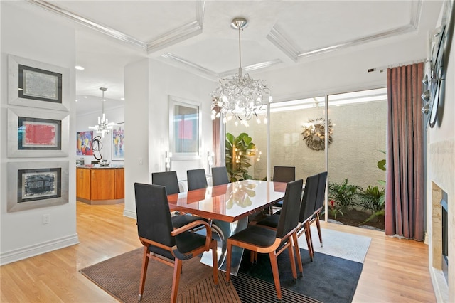 dining area featuring light wood-style flooring, coffered ceiling, a glass covered fireplace, an inviting chandelier, and crown molding