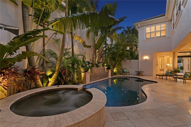 pool at twilight featuring a patio area, a pool with connected hot tub, and a fenced backyard