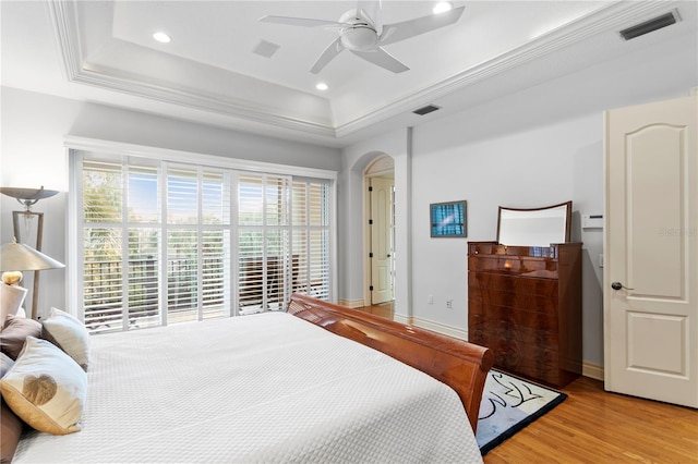 bedroom featuring light wood finished floors, visible vents, a tray ceiling, recessed lighting, and arched walkways