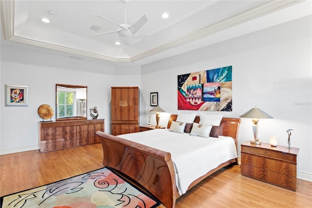 bedroom with a tray ceiling, wood finished floors, recessed lighting, crown molding, and baseboards