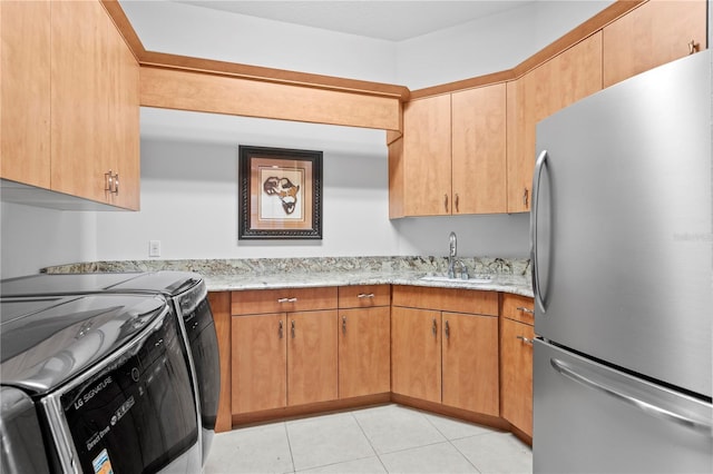 kitchen with a sink, freestanding refrigerator, separate washer and dryer, light tile patterned floors, and light stone countertops