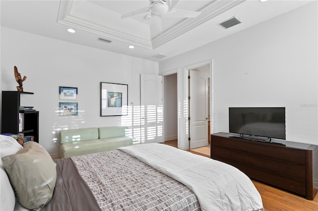 bedroom with a tray ceiling, visible vents, light wood finished floors, and ornamental molding