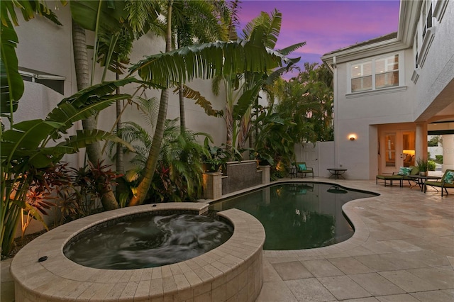 pool with an in ground hot tub, a patio area, and fence