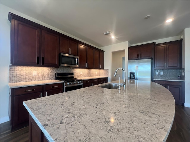 kitchen with a spacious island, light stone countertops, stainless steel appliances, and a sink