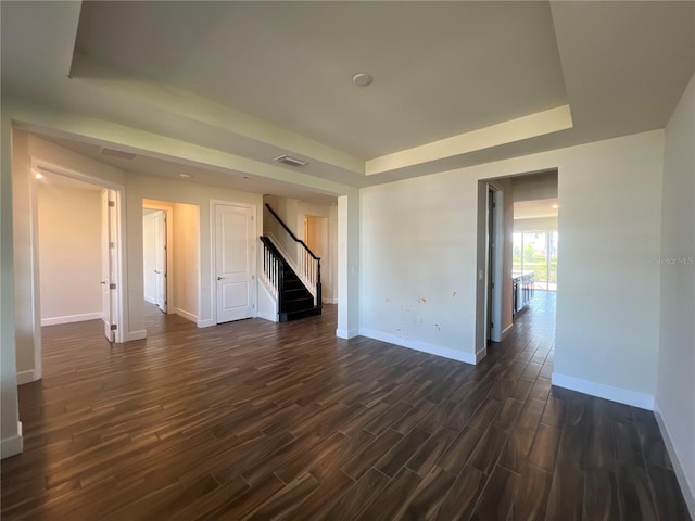 empty room featuring stairway, baseboards, visible vents, a tray ceiling, and dark wood-type flooring