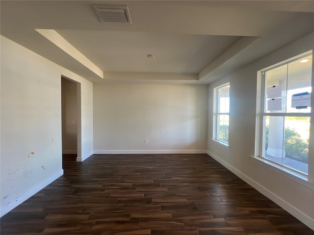 unfurnished room with dark wood finished floors, a tray ceiling, baseboards, and visible vents