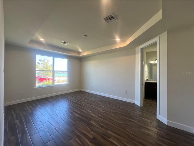 spare room with visible vents, a raised ceiling, baseboards, and dark wood finished floors