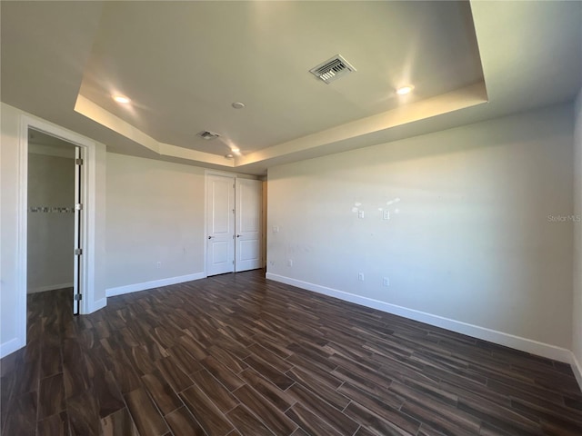 empty room with dark wood finished floors, a raised ceiling, baseboards, and visible vents