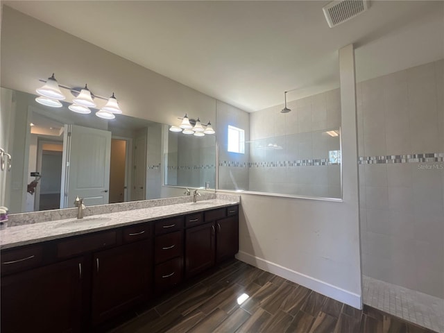 bathroom with double vanity, visible vents, a walk in shower, and a sink