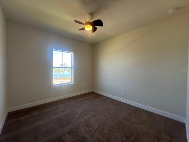 spare room with dark carpet, a ceiling fan, and baseboards