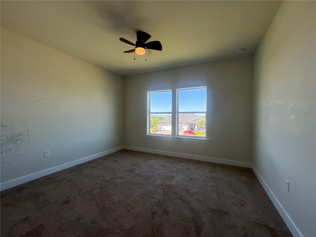 empty room featuring dark carpet, baseboards, and ceiling fan