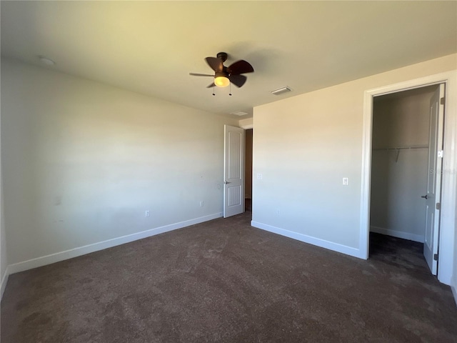 unfurnished bedroom featuring visible vents, a walk in closet, a closet, dark colored carpet, and baseboards