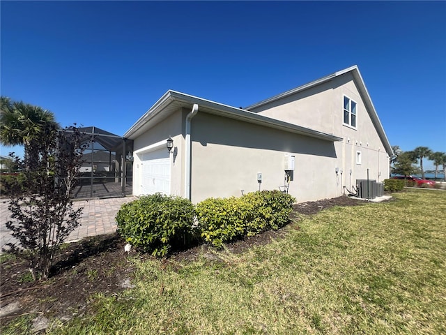 view of property exterior featuring glass enclosure, central AC unit, stucco siding, a garage, and a lawn